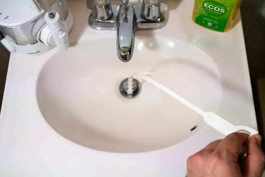 using a plumbing snake to clear a clogged drain in a sink